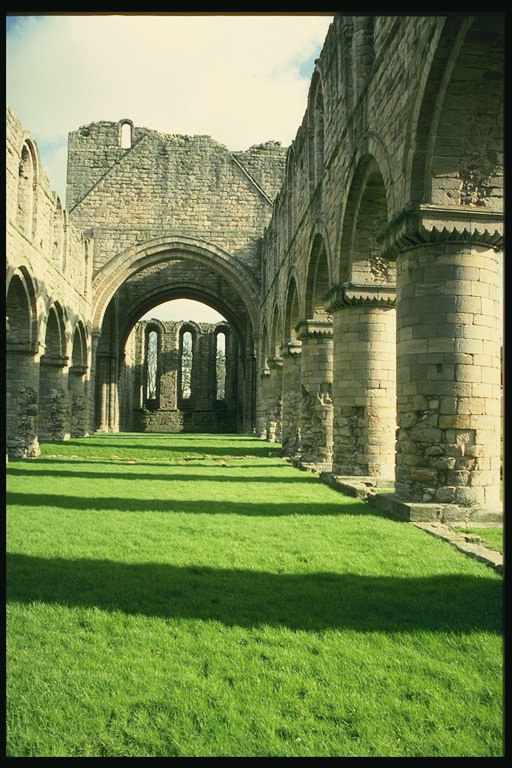 Outdoor corridor forms of arches supporting columns and manicured green meadow