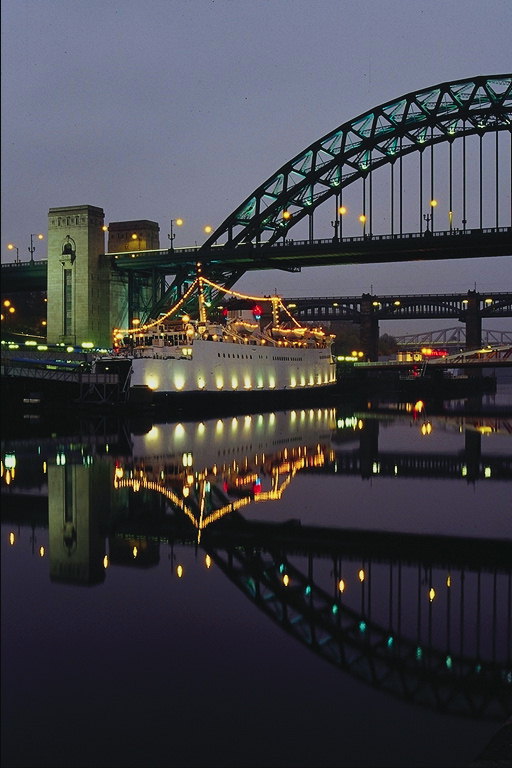 Освещённый корабль проходит ночью под мостом