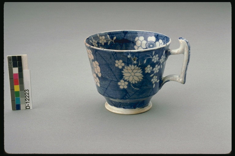 Tumman sinistä kupin, jossa on valkoinen kahva ja valkoiset kukat