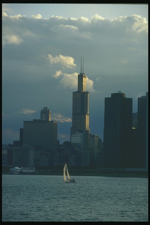 Evening is time on the shore of Lake Michigan where a lone sail gliding through the water on the background of skyscrapers