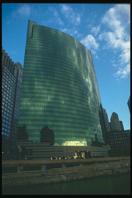 Полукруглое высокое здание зелёного оттенка из золотым отблеском солнечных лучей вечернею порою