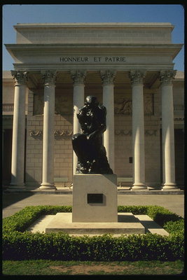 Скульптура мужчины у входа в здание с колонами