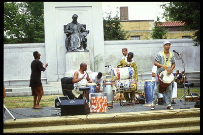 Группа музыкантов играют на музыкальных инструментах перед памятником