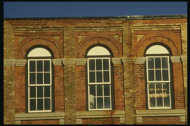 Архитектурное изящество окон в виде арки. Фасад здания построен из красного и коричневого кирпича