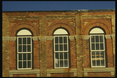 Архитектурное изящество окон в виде арки. Фасад здания построен из красного и коричневого кирпича