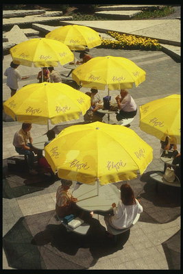 Под жёлтыми зонтиками прохожие отдыхают и пьют кофе 