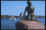Скульптура русалки сидящей на камне и смотрящей вдаль на море