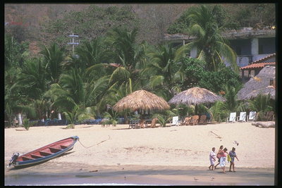 Лодка на песчаном берегу, где прогуливаются отдыхающие люди