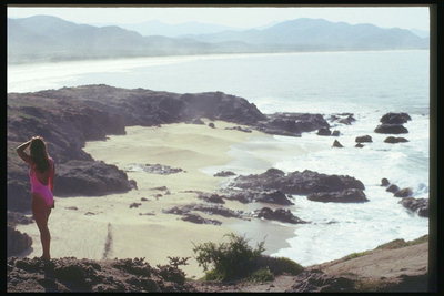 Chica a la orilla rocosa de una playa desierta adorna rocosos