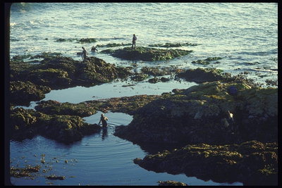 Orang mandi di laut di antara batu