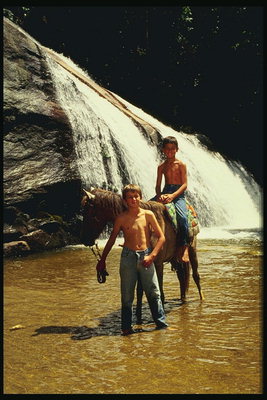 Duas crianças em um cavalo de pé em um lago de montanha