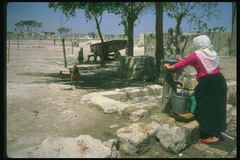 Женщина набирающая воду с колонки