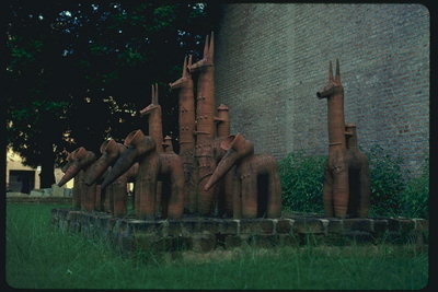 Скульптуры из глины животных стоящих в саду возле стены здания