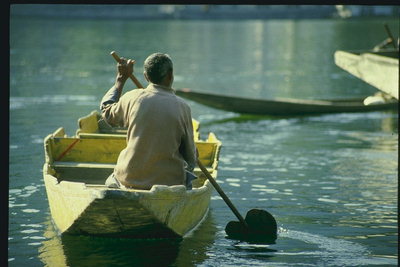 Мужчина плывущий на лодке с веслом через реку