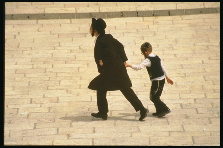 Мужчина ведёт мальчика за руку по площади