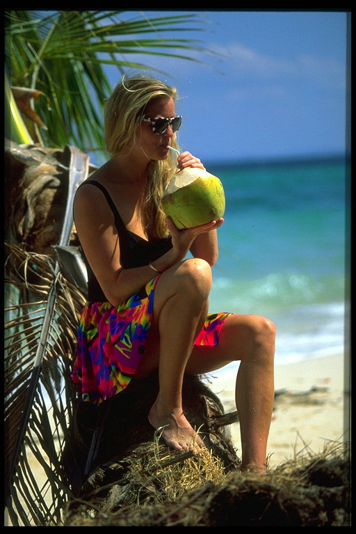 Женщина на берегу пьёт сок тропического фрукта