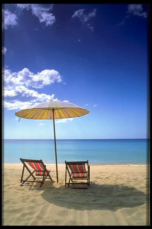 Два лежака и зонтик против солнца на песчаном берегу