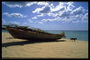 Лодка стоит на песчаном берегу укрытая листьями от солнца