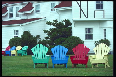 Красный, желтый, синий, зеленый стульчики на лужайке у дома