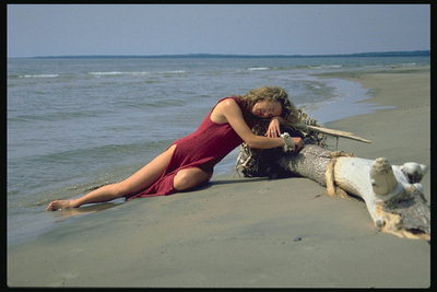 Девушка в бордовом платье на мокром песку. Бревно дерева