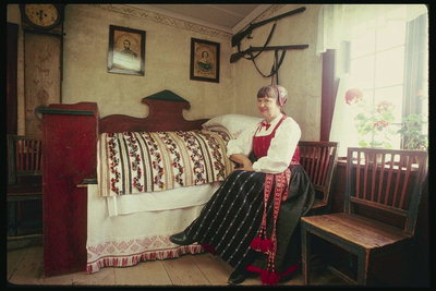 Пожилая женщина в чепчике. Кровать с вышитым покрывалом