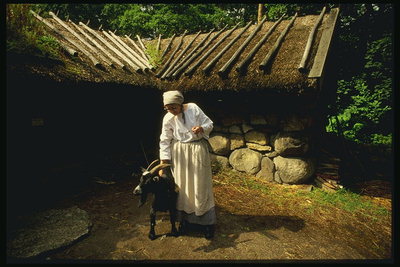 Женщина и козел у домика с соломенной крышей