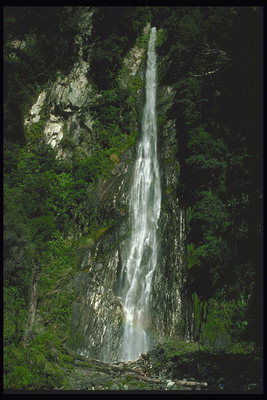 Водопад среди горных пород и зеленых деревьев
