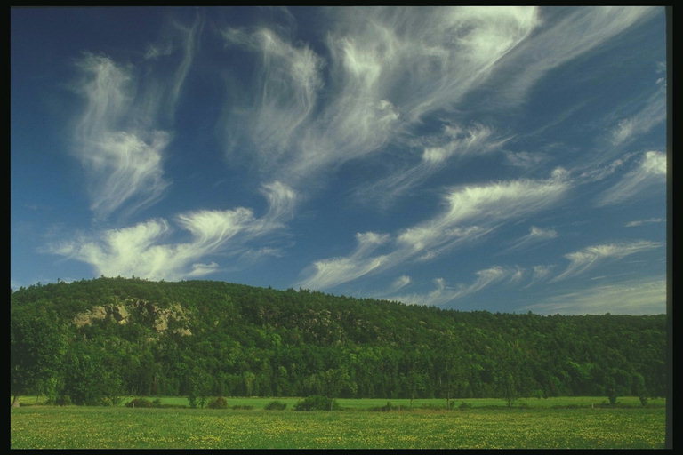 Волнообразные облака на фоне темно-зеленых гор