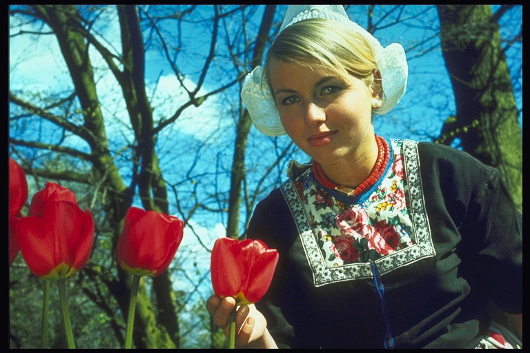 Frau im roten Kleid mit nationalen Tulpen auf dem Hintergrund eines nackten Bäume