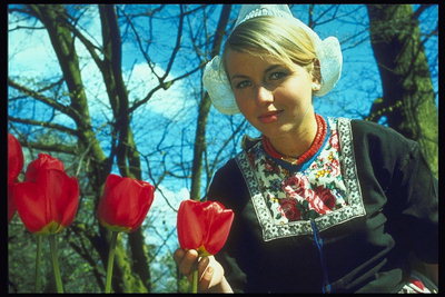 Vrouw in de nationale jurk met rode tulpen op een achtergrond van kale bomen
