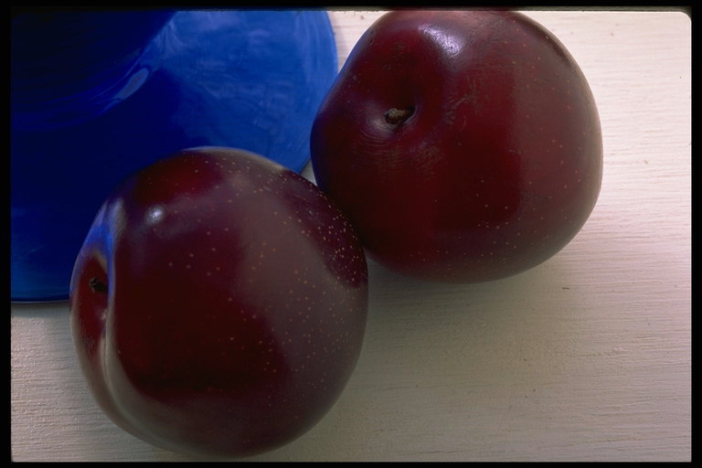 Темно-бордовые плоды яблок возле темно-синей вазы