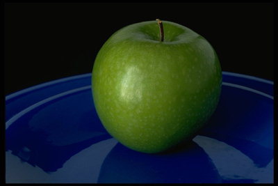 Зеленое яблоко в керамической тарелке темно-синего цвета
