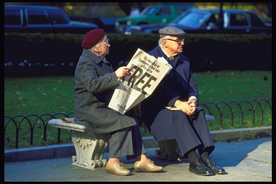 Пожилые люди читают на лавочке газету