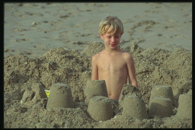 Berniukas daro su smėlio pilis