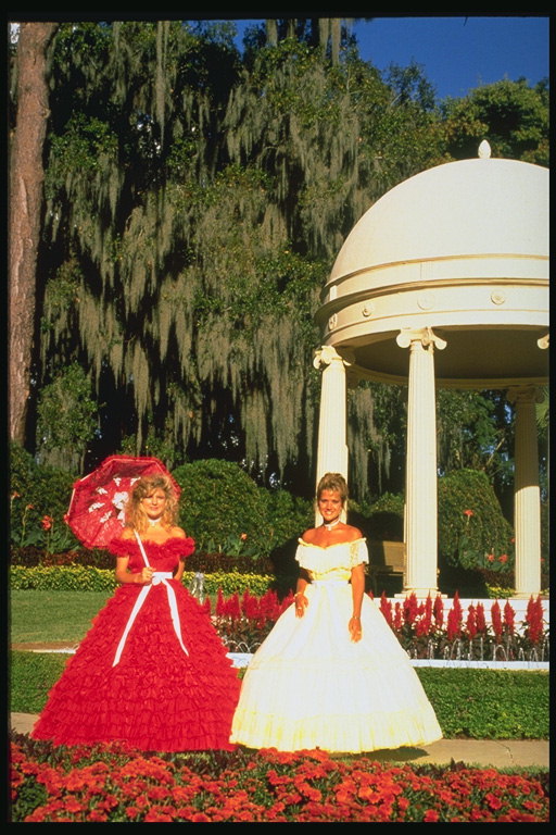 Kvinder i flotte kjoler med paraply for en tur