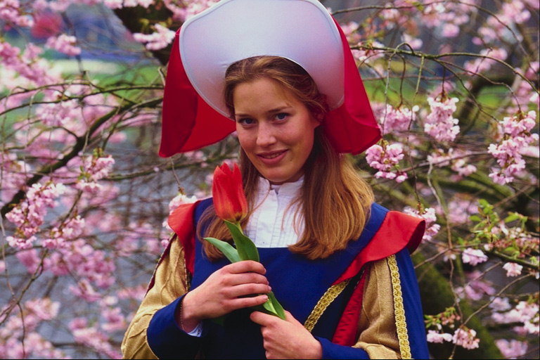 Girl in drakt i hatten med en rød tulipan i hendene på