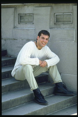 Veselă tânăr într-un alb pulover tricotat şedinţei de pe scari