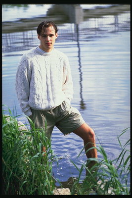 A young guy in shorts stands in the water near the coast