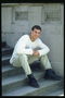 Veselý mladý muž v bílém pletený svetr sedí na schodech