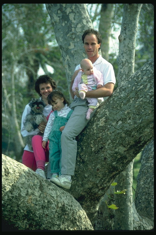 Far og tre barn mellom trærne
