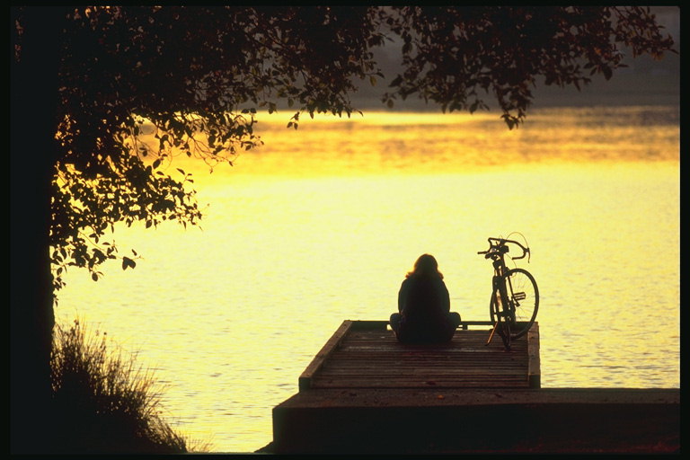 Njeriu me biçikletë në breg lumi