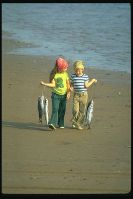 Barn med en fisk i hendene på stranden