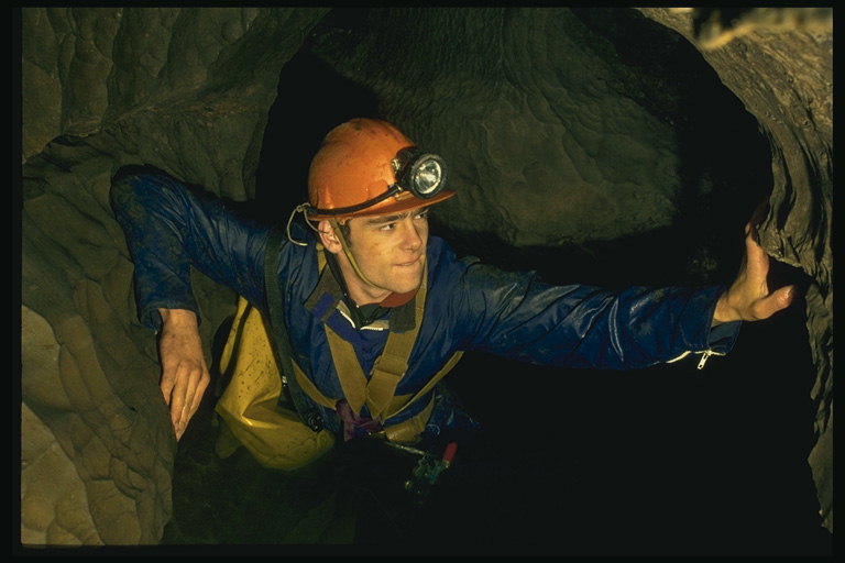 Muž v přilbě s baterkou v tunelu