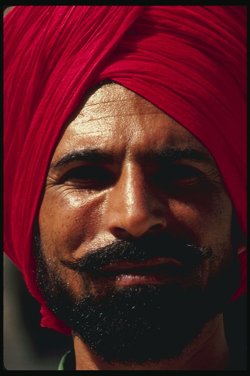 Un uomo con un turbante rosso scuro. Barba nera corta