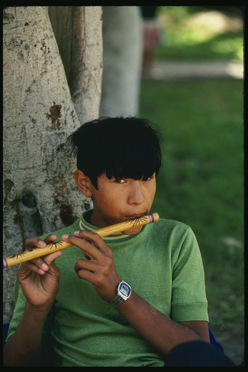 Chlapec s dreveným hudobným nástrojom pod stromom