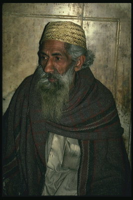 Një njeri në një mantel ngjyrë kafe të errët kundër sfondit të një mur guri