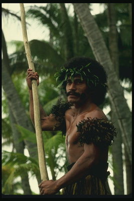 Seorang pria mengenakan karangan bunga daun hijau dan tebal tongkat