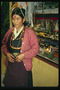 Une femme en jupe à rayures et de perles multicolores. Un point rouge sur le front