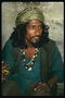 A man in a dark green shirt, a turban with a brilliant thread, and beads with colorful stones