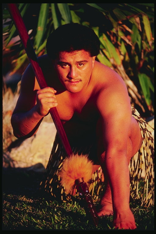Um homem com uma lança em suas mãos e com uma saia de folhas secas